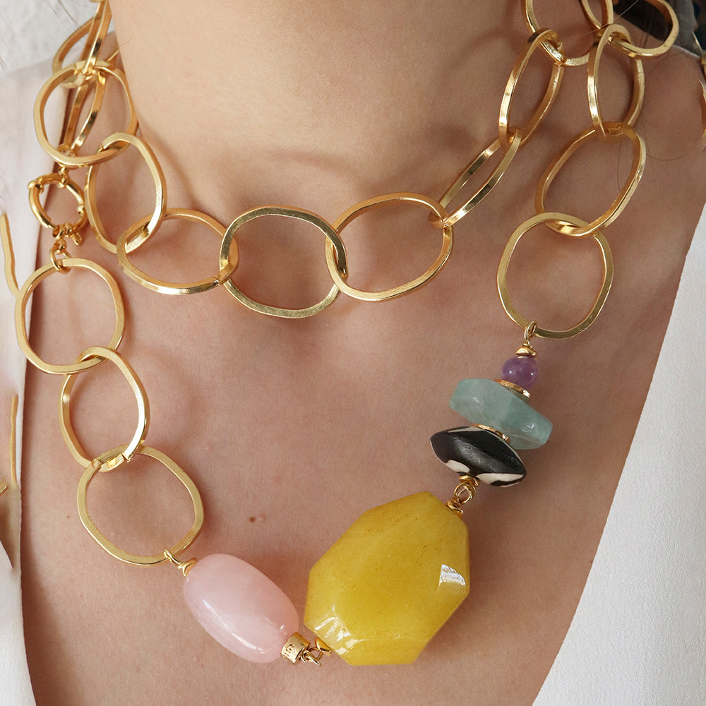 Collar dorado con eslabones grandes y piedras de colores, ámbar, rosa, azul y negro, estilo moderno y elegante.
