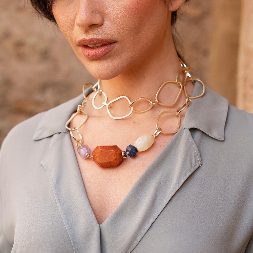 Collar dorado de eslabones con piedras semipreciosas en tonos naranja, morado y blanco, estilizado y moderno.