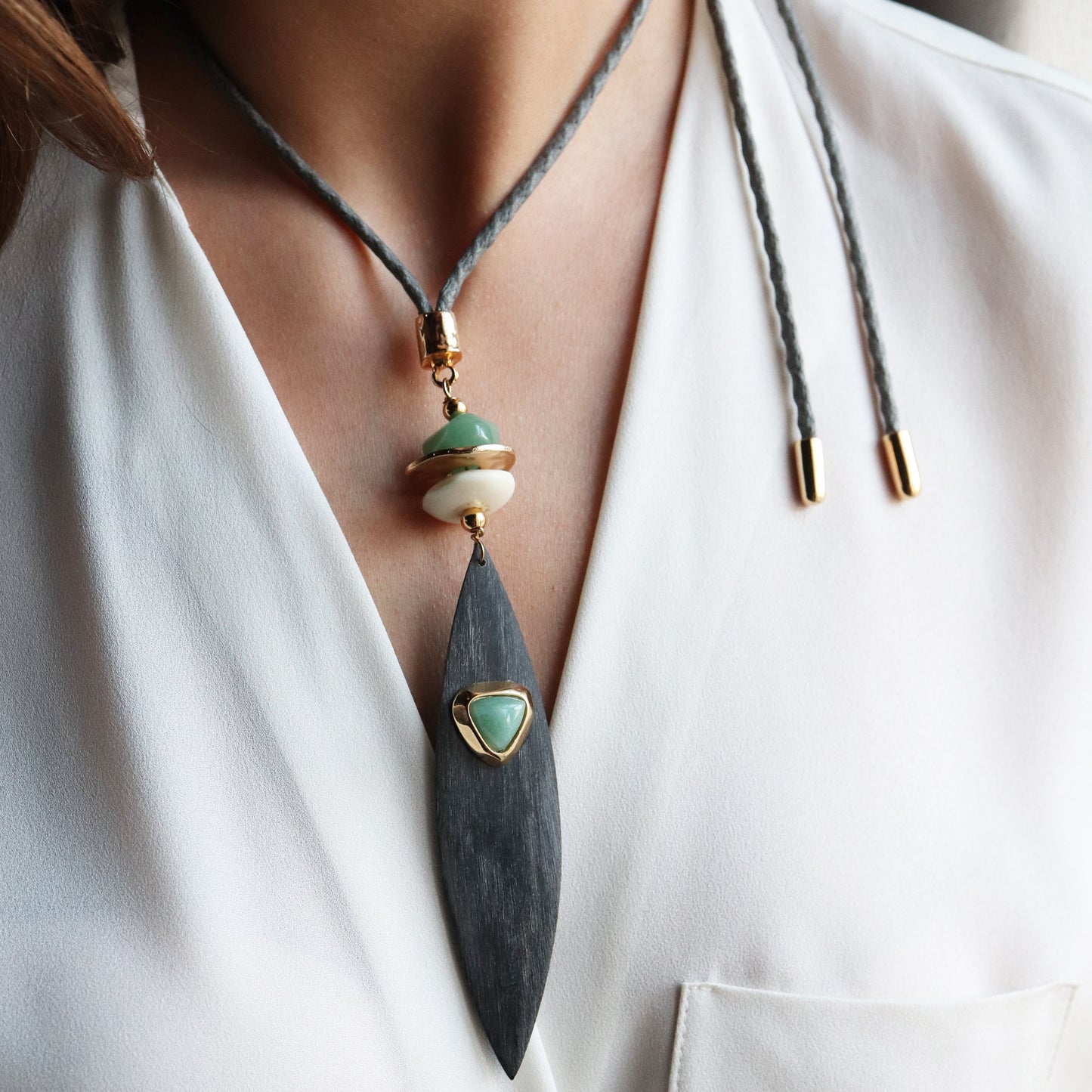 Collar elegante con colgante negro, piedras verdes y doradas, cuerda gris, estilo bohemio. Ideal para ocasiones especiales.