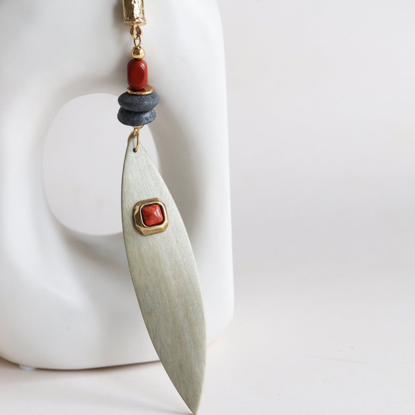 Aretes de metal en forma de hoja con detalles en rojo y gris, estilo moderno y artesanal.