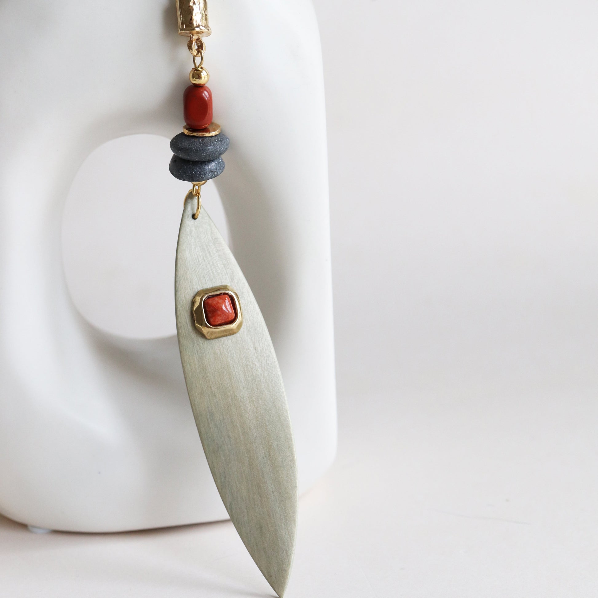 Aretes de metal en forma de hoja con detalles en rojo y gris, estilo moderno y artesanal.
