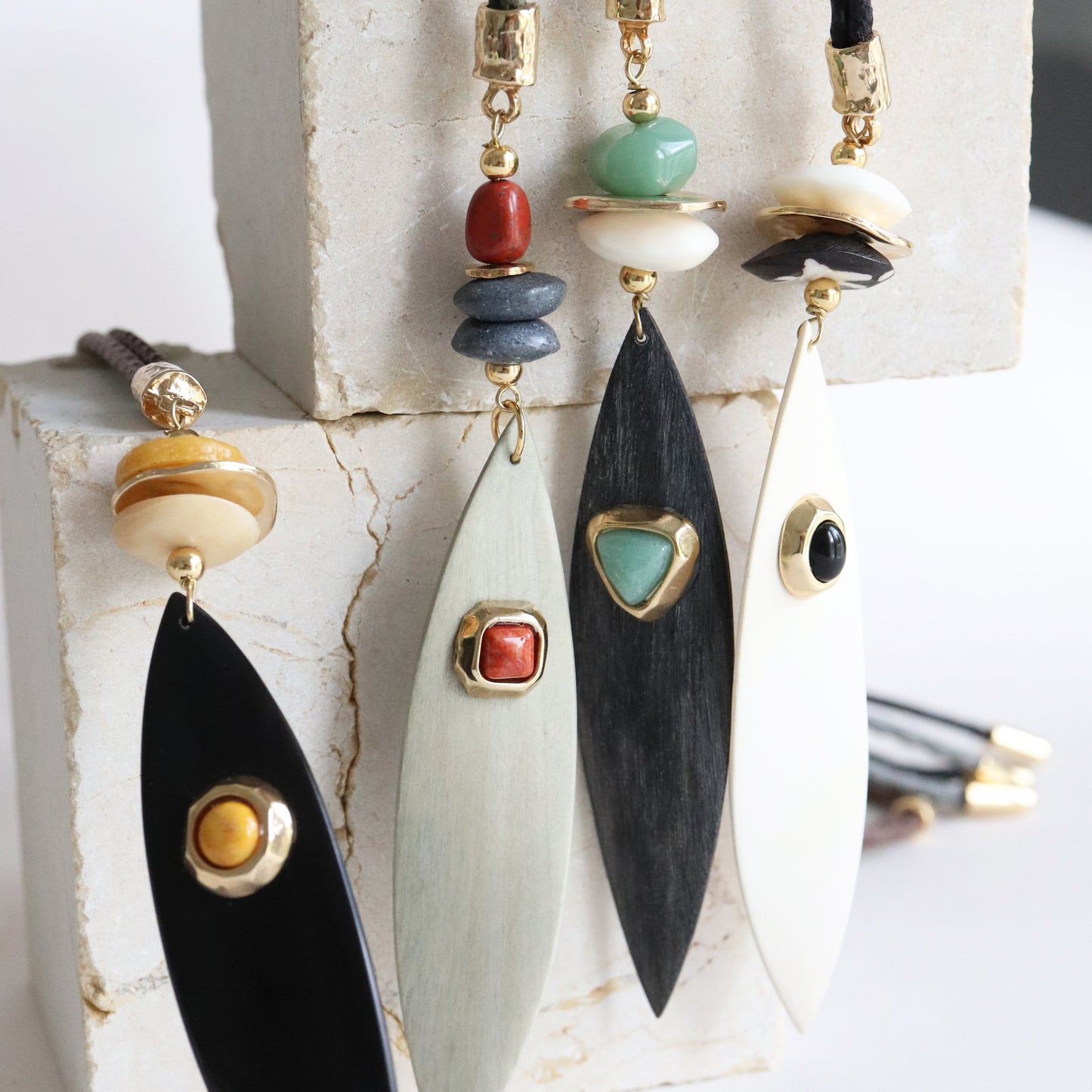 Collares elegantes con colgantes en tonos negro, blanco y dorado, decorados con piedras preciosas y materiales naturales.