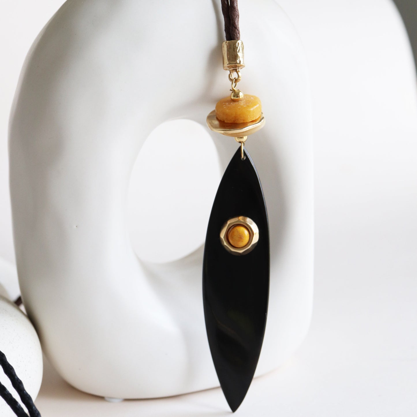Collar de diseño moderno con colgante negro, cuentas doradas y cordón de cuero marrón. Ideal para un look elegante.