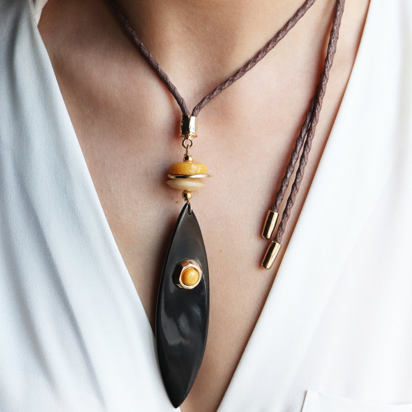 Collar de cuero marrón con colgante negro y dorado, estilo moderno y elegante.