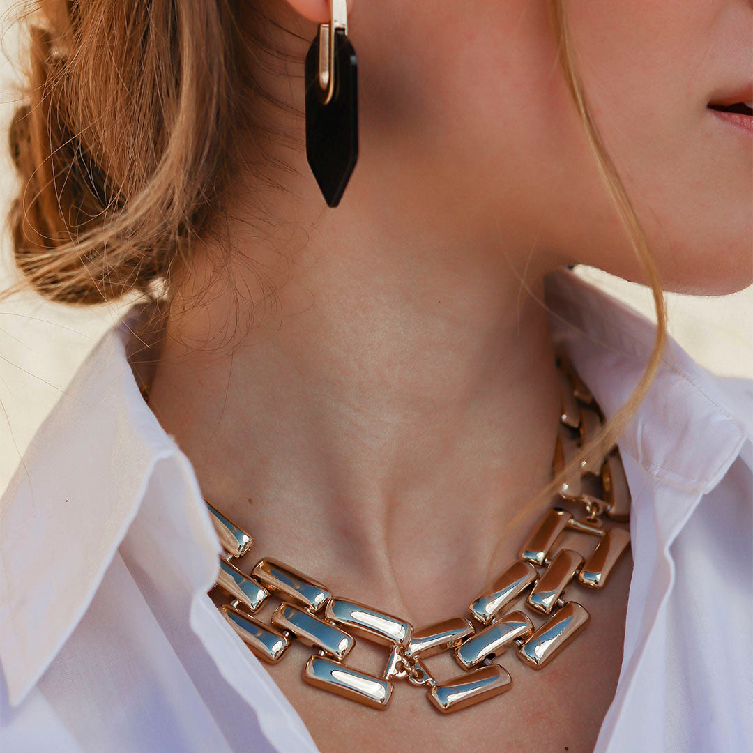 Collar de eslabones dorados con aretes negros, estilo elegante y moderno, ideal para ocasiones especiales.