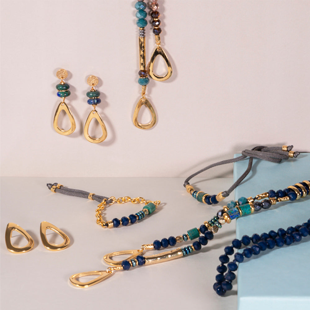 Conjunto de joyería dorada con piedras azules y verdes, incluye aretes, pulsera y collar elegante.