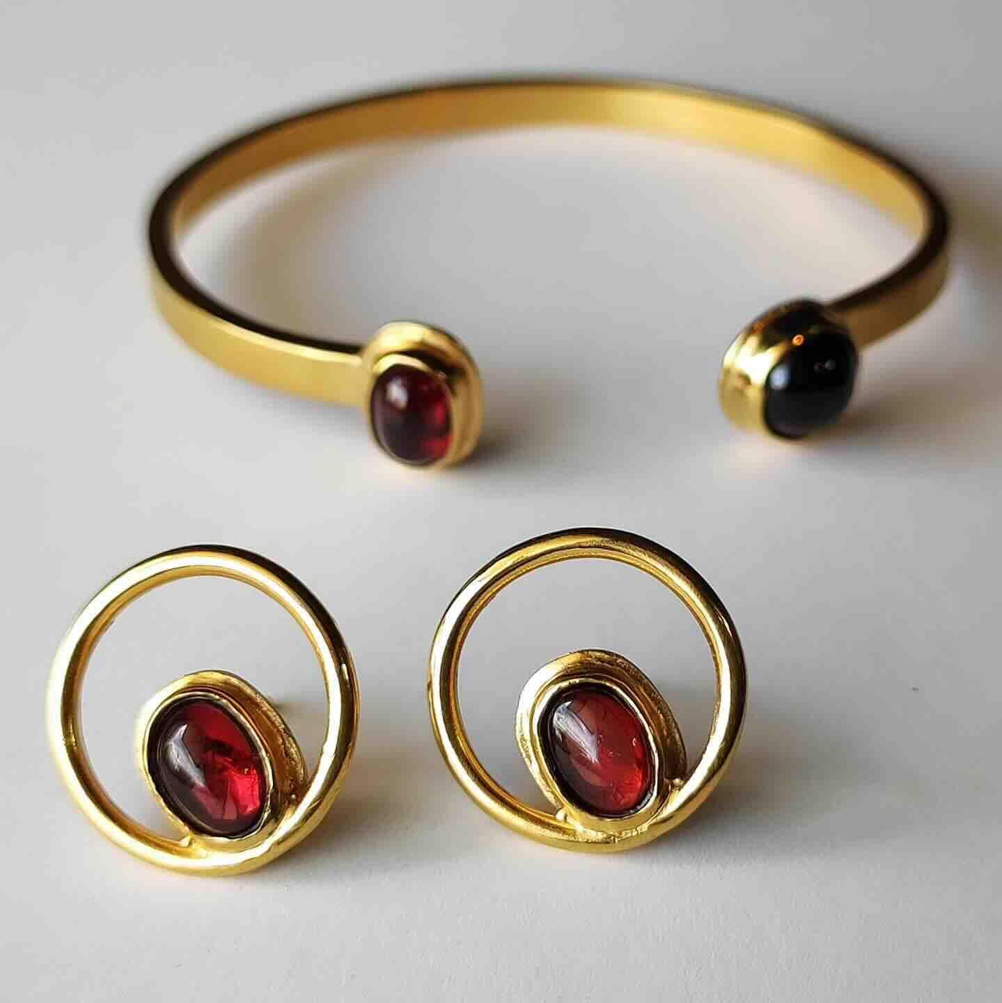 Gold cuff bracelet and matching circular earrings with garnet and onyx gemstones, featuring a modern and elegant design.
