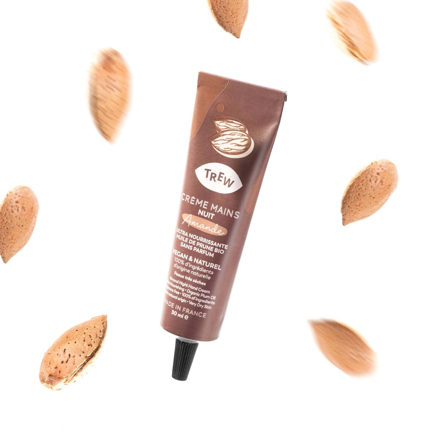 Brown tube of Crème mains nuit surrounded by floating almonds on a white background.