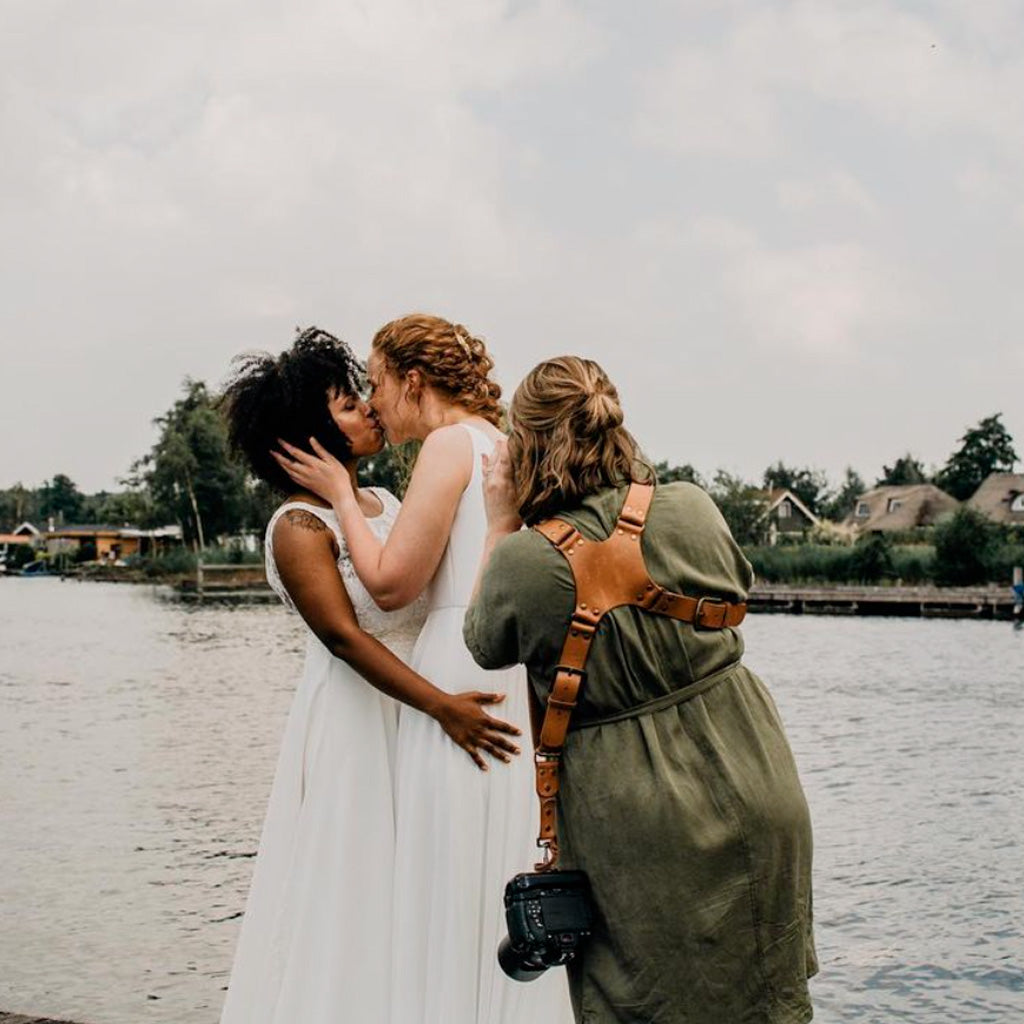 Handmade dual leather camera strap in use during wedding photoshoot with brides by the water.