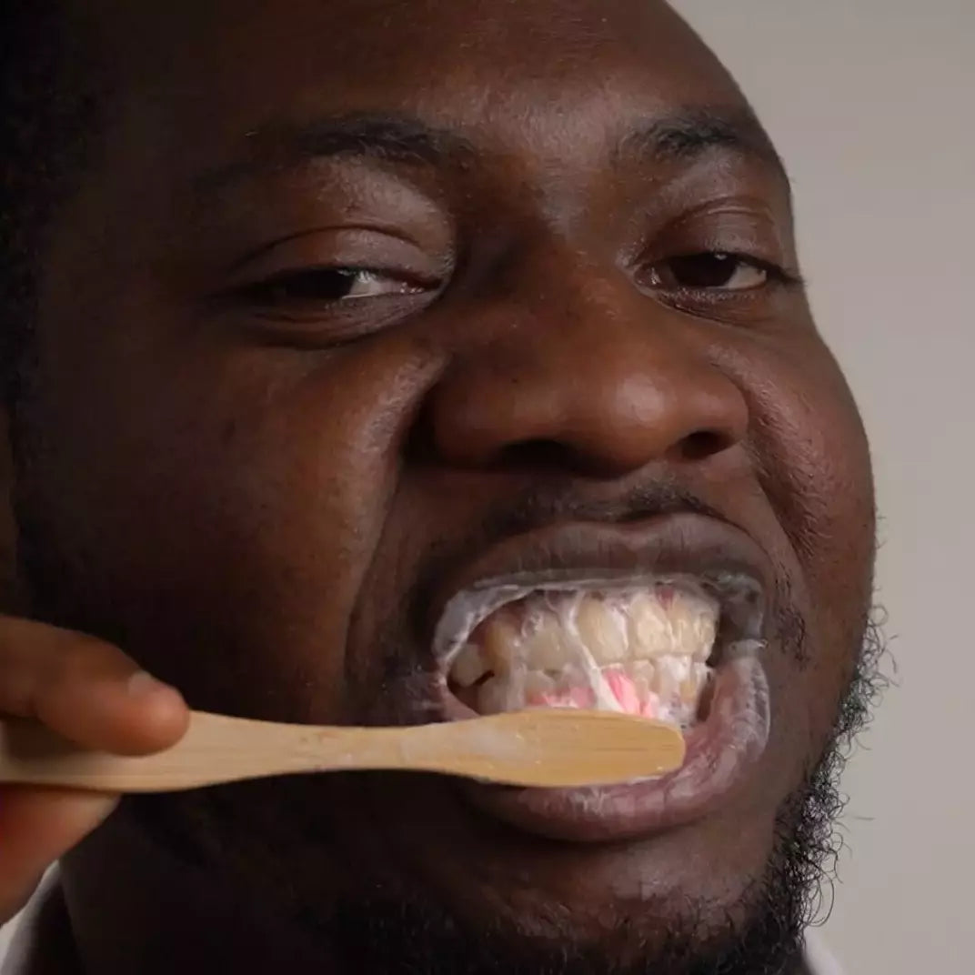 Homme se brossant les dents avec une brosse en bois et le dentifrice Trew Cosmetic à la texture crémeuse rose et blanc.