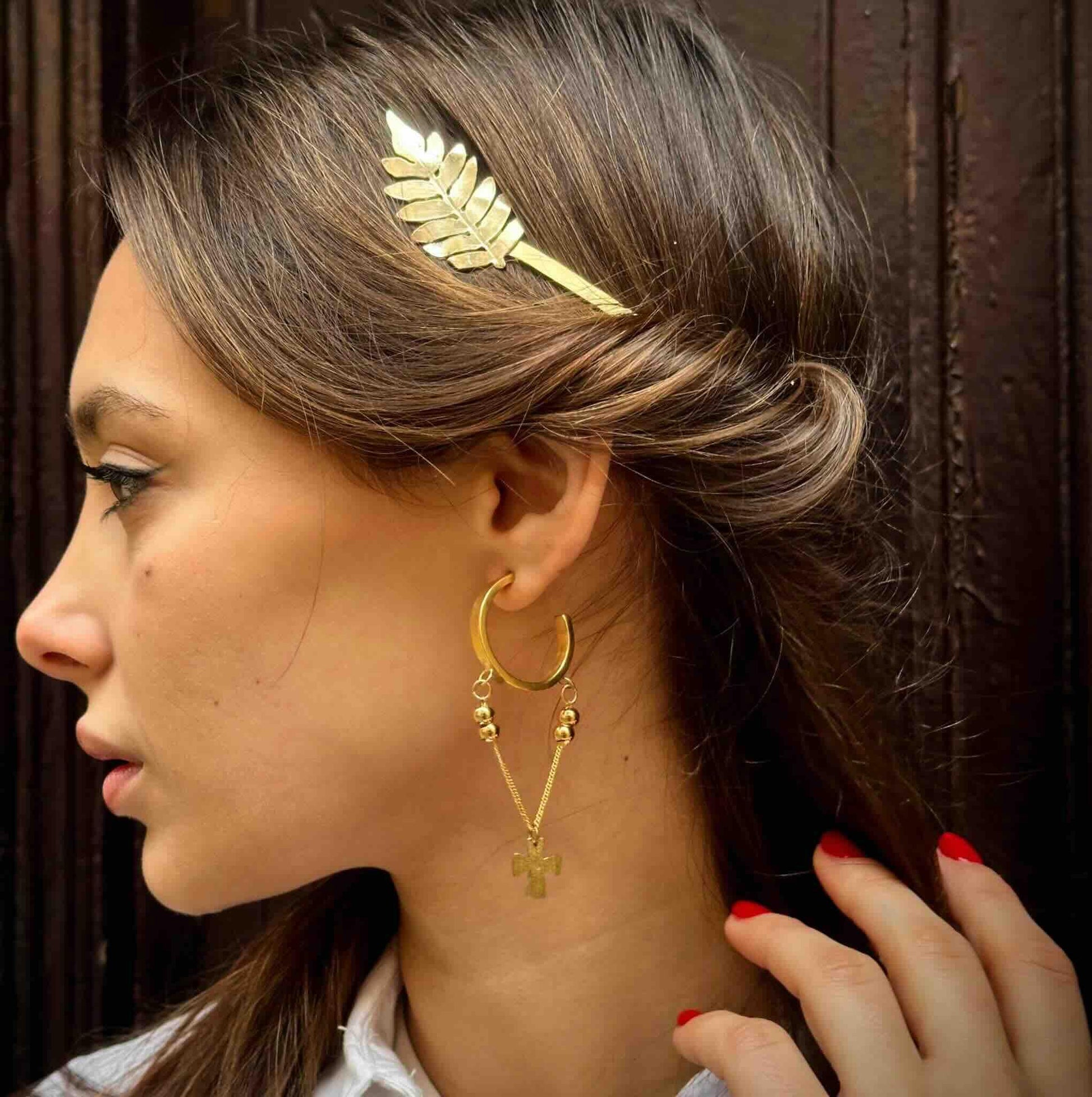 Accesorio de cabello dorado con diseño de hoja y pendientes de cruz dorados, estilo elegante y moderno.