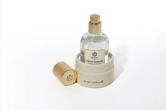 Cherry Gourmet extrait de parfum bottle in a round beige box, with a separate gold cap on a white background.