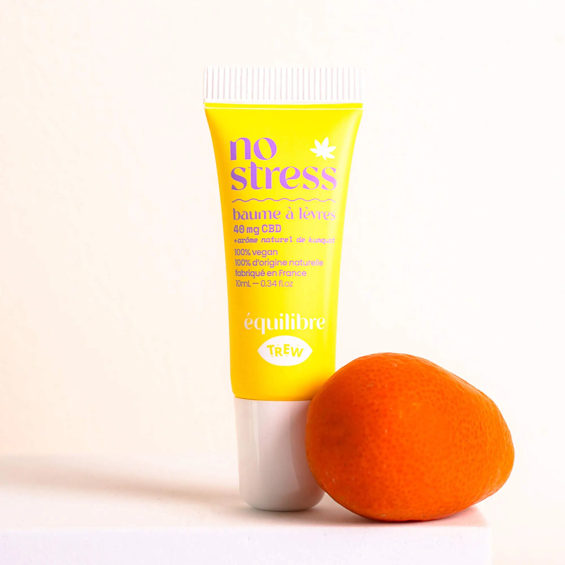 Yellow squeeze tube of CBD lip balm with purple text, standing next to a fresh kumquat on a white surface.