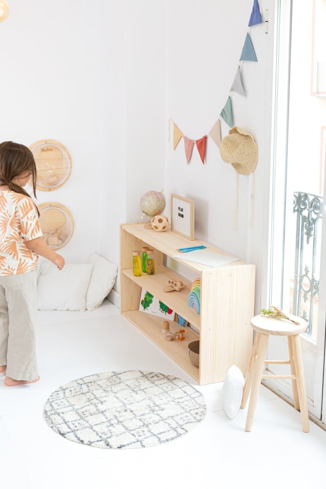 Estantería de madera clara con estantes abiertos, decorada con objetos coloridos, ideal para habitaciones infantiles.