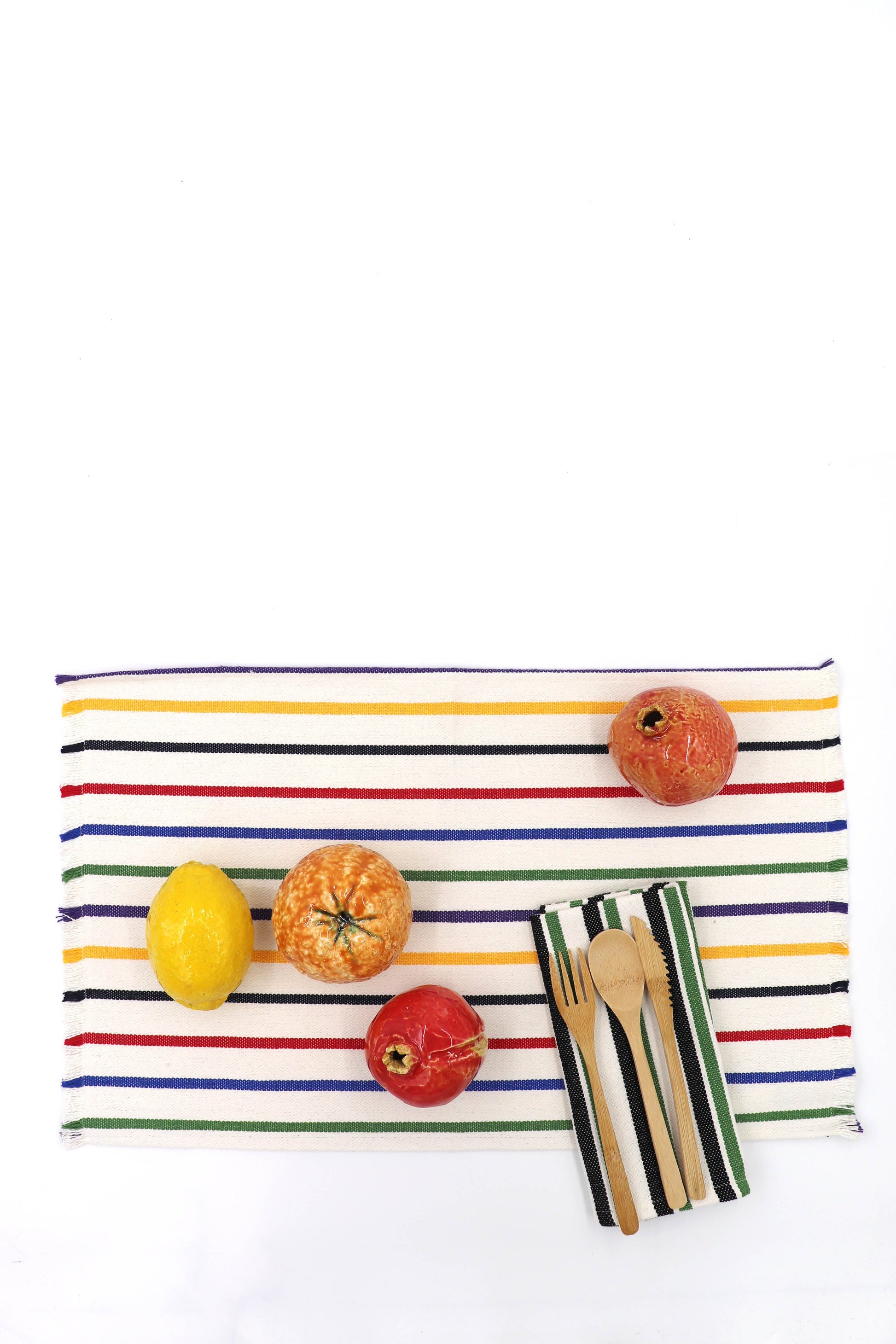 Mantel de rayas amarillo, rojo y azul con frutas y utensilios de madera, ideal para mesa de cocina.