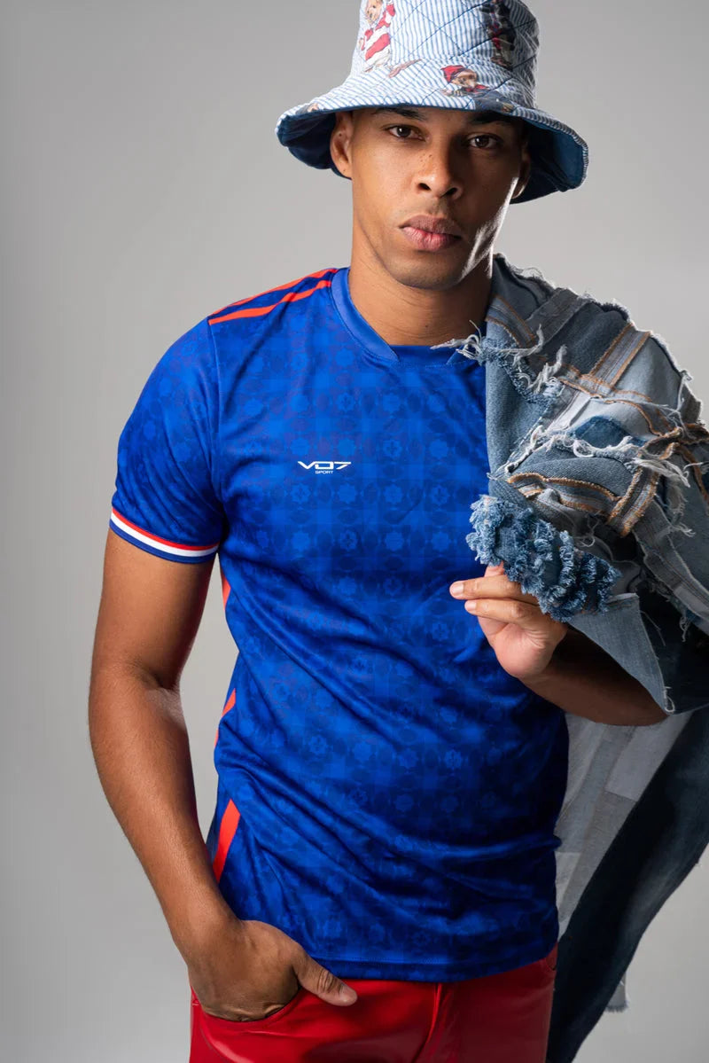 Maillot bleu VO7 technique à motifs, logo blanc et détails tricolores aux manches, porté par un mannequin.