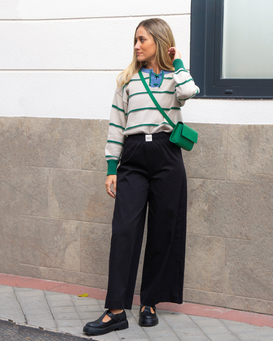 Suéter a rayas beige y verde con pantalones anchos negros, combinado con bolso verde y zapatos negros.