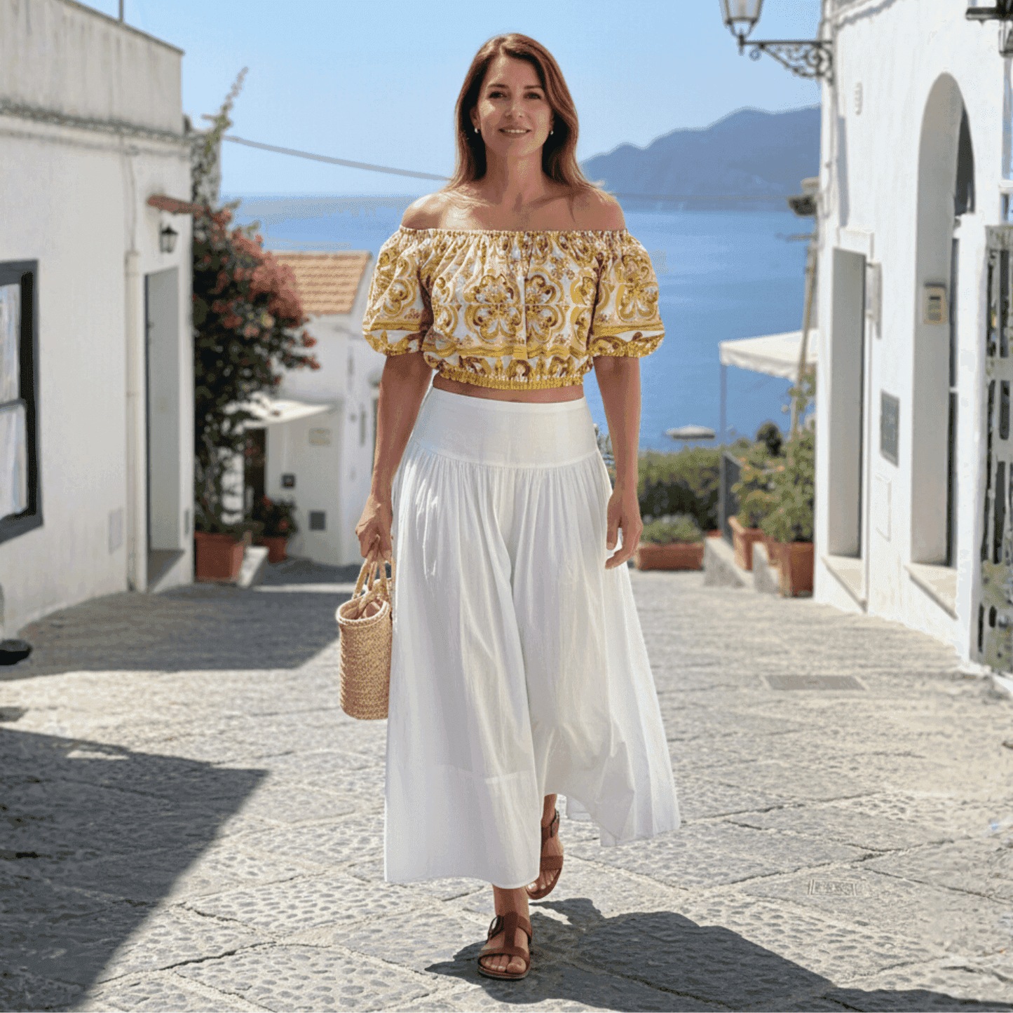 Off-the-shoulder cotton crop top with yellow and white Mediterranean majolica tile print, worn with a white maxi skirt.