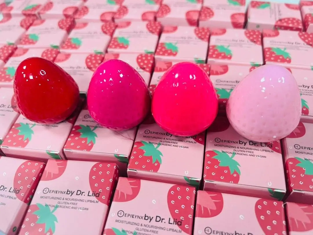 Four strawberry-shaped lip butter pods in red, magenta, hot pink, and light pink sitting atop matching boxes.