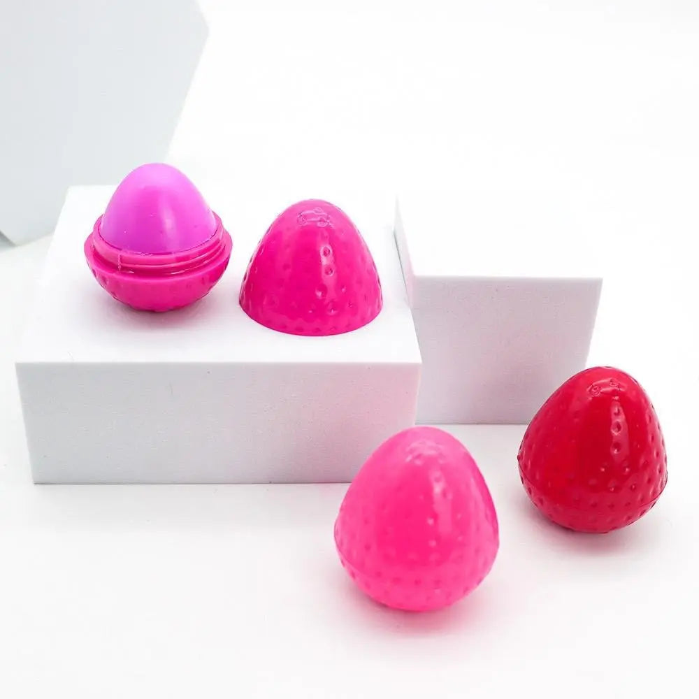 Strawberry-shaped lip butter containers in bright pink and red, displayed on white geometric platforms.