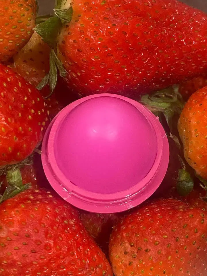 Bright pink, dome-shaped lip butter nestled amongst fresh, ripe strawberries.