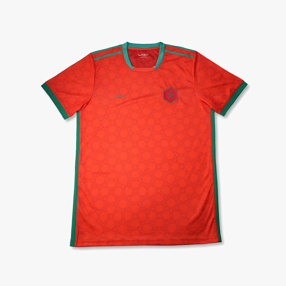 Maillot de sport rouge VO7 à motifs géométriques, col et bords verts, avec écusson en forme d'hexagone sur la poitrine.
