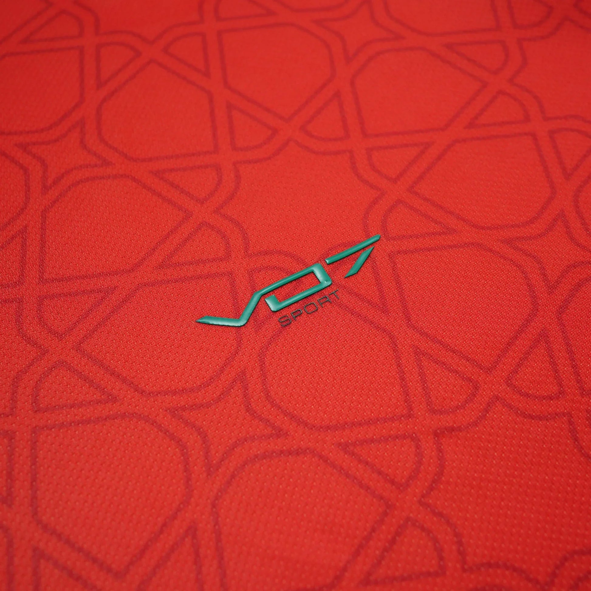Maillot rouge VO7 en tissu technique, orné d'un motif géométrique ton sur ton et du logo VO7 Sport en vert émeraude.