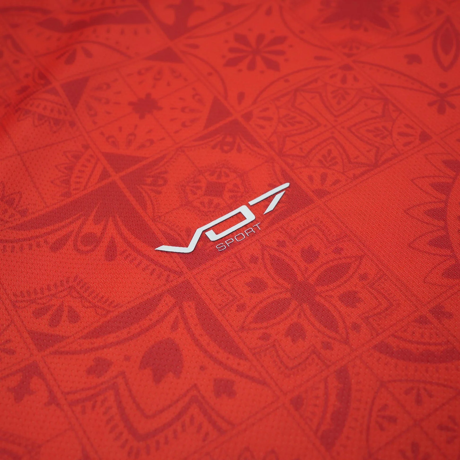 Maillot VO7 rouge en tissu technique à motifs géométriques et floraux, avec logo blanc contrasté au centre.