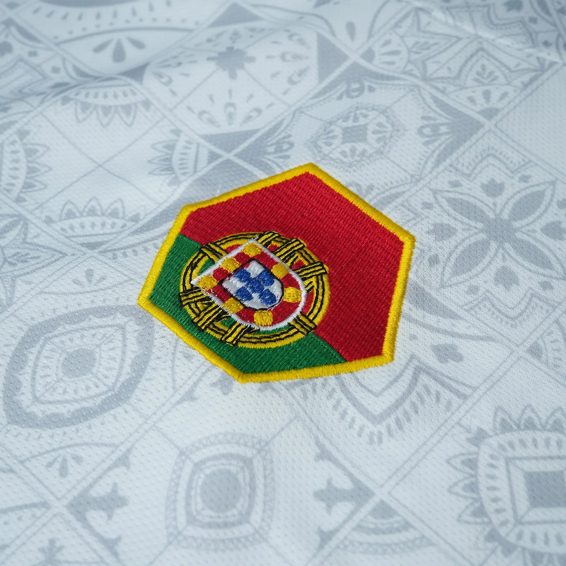 Maillot blanc VO7 à motif azulejos gris, avec un écusson hexagonal brodé aux couleurs du Portugal : vert, rouge et or.