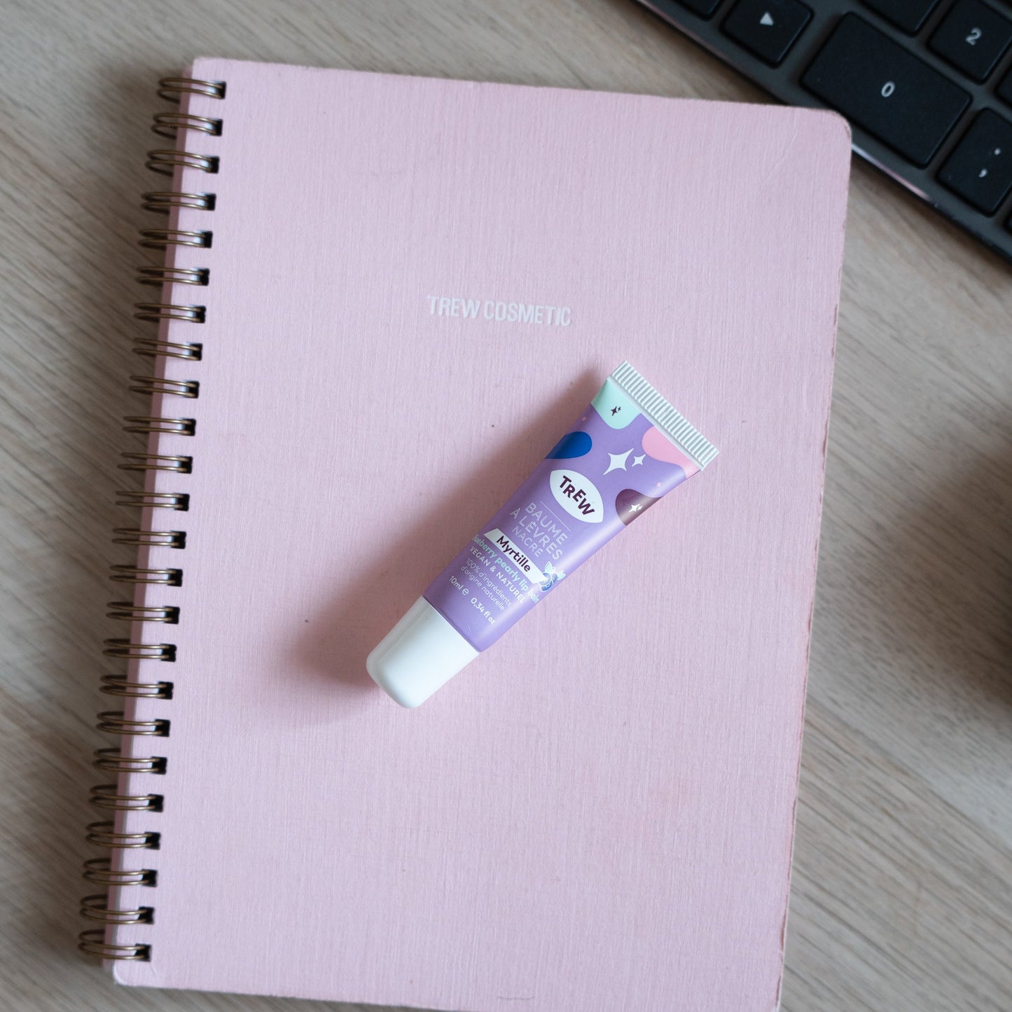 Purple, star-patterned blueberry tinted lip balm tube resting on a pink spiral notebook.