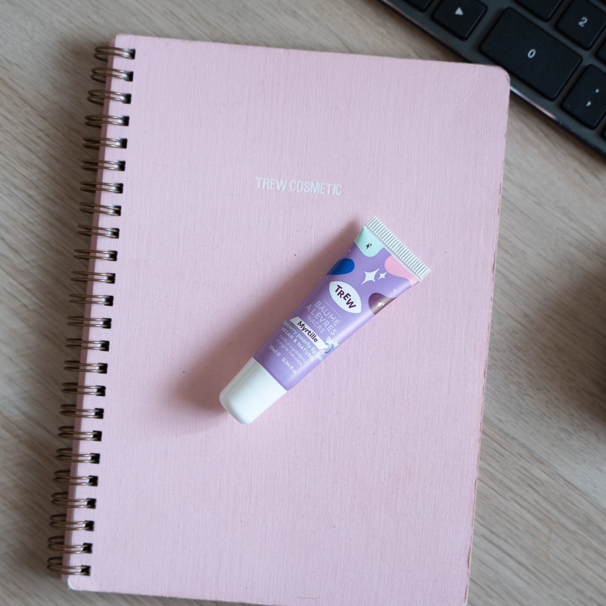 Purple, star-patterned blueberry tinted lip balm tube resting on a pink spiral notebook.