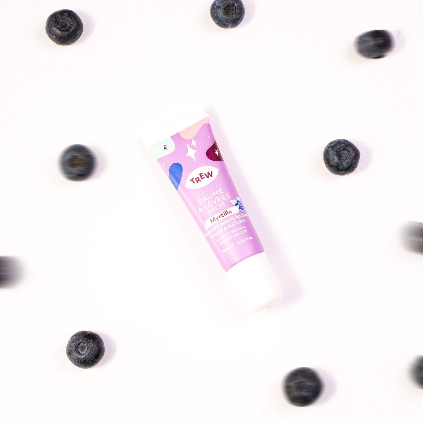A tube of blueberry pearly lip balm surrounded by scattered fresh blueberries on a white background.