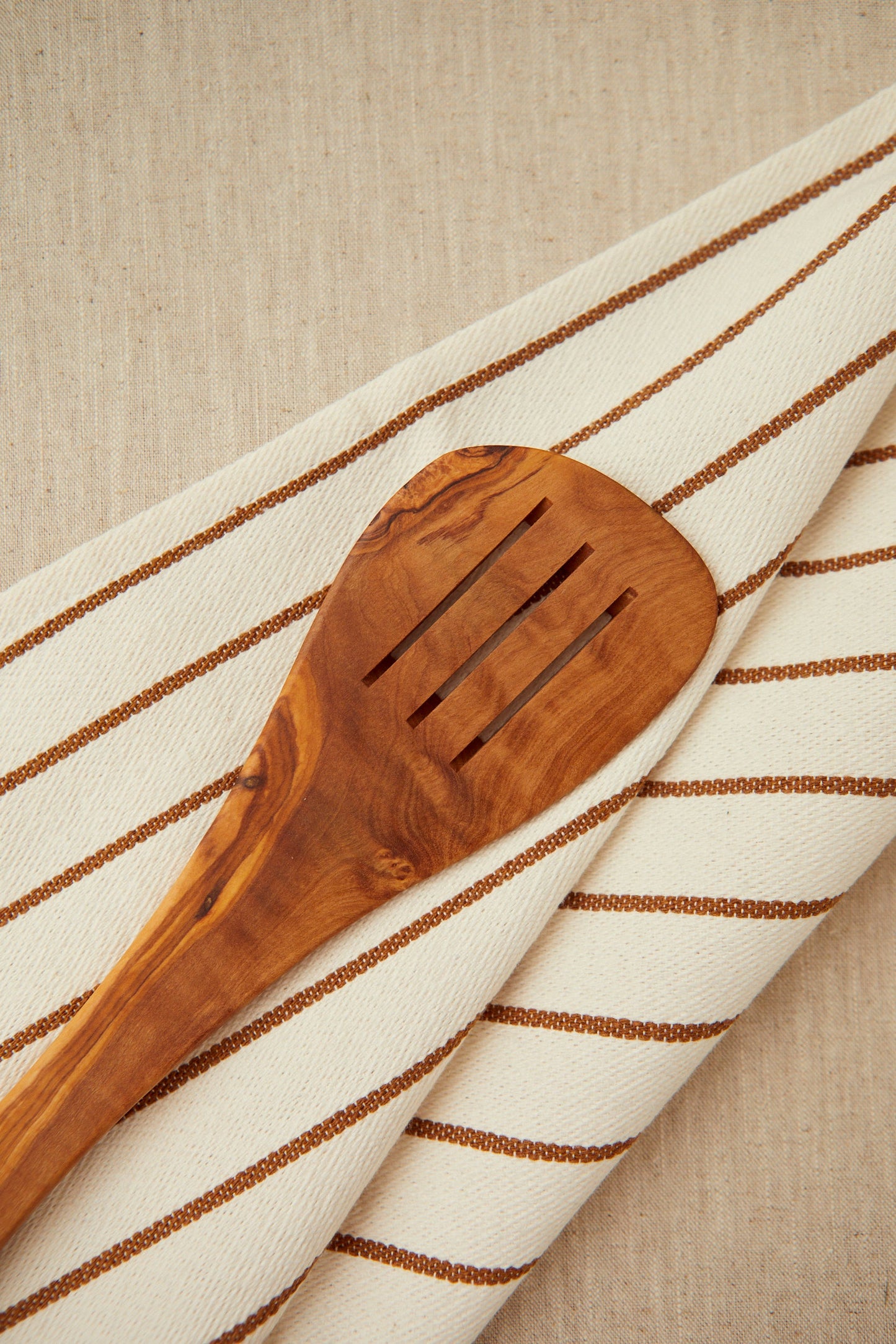 Espátula de madera de olivo con diseño ranurado, sobre un paño beige con rayas marrones.