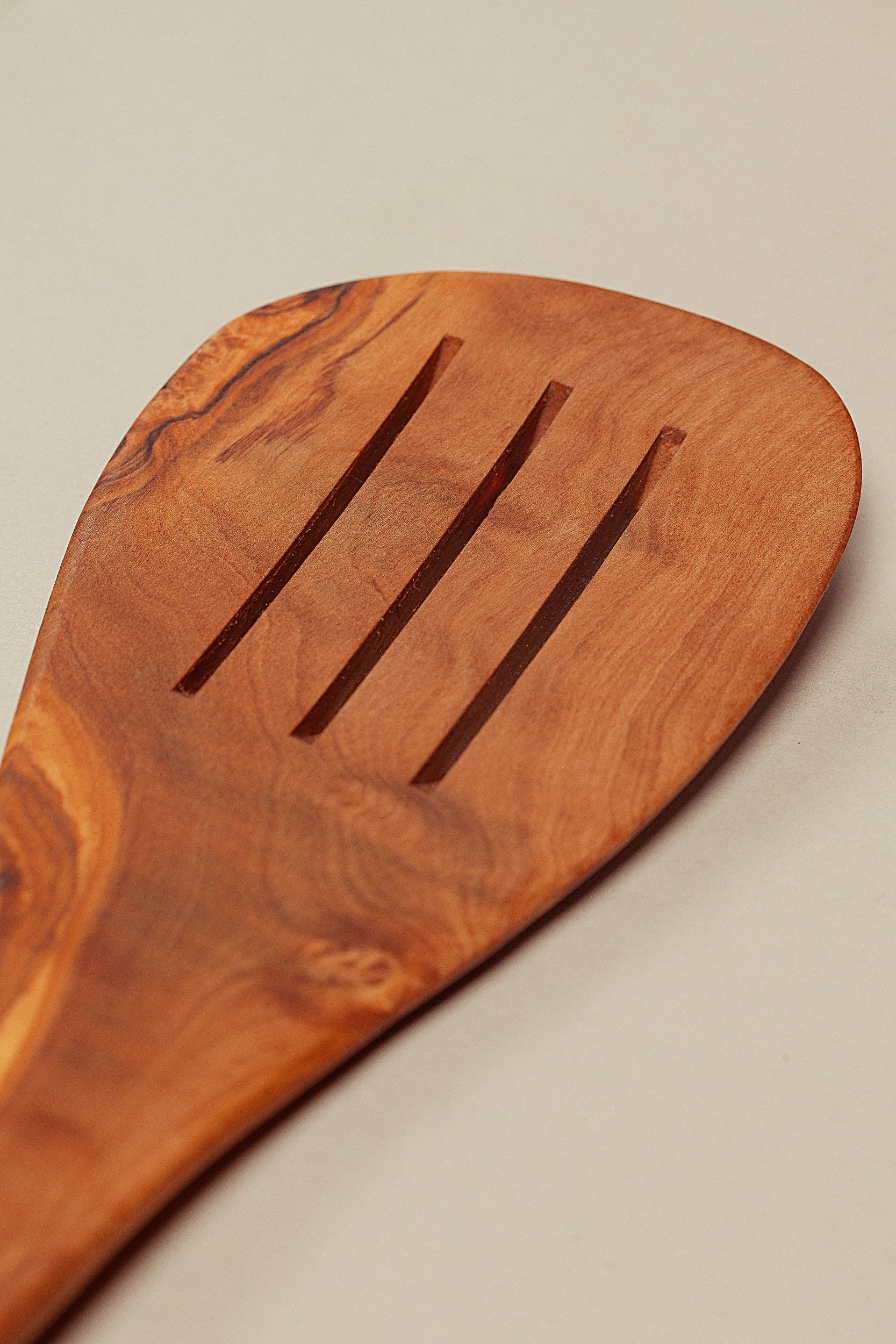 Espátula de madera de olivo con diseño pulido y ranuras, color marrón natural, ideal para cocinar.