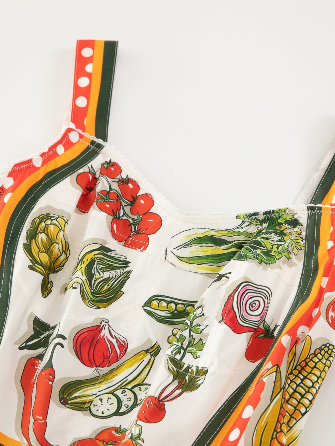 Colorful vegetable-print sleeveless blouse with lace trim, featuring vibrant greens, reds, and yellows on a white background.