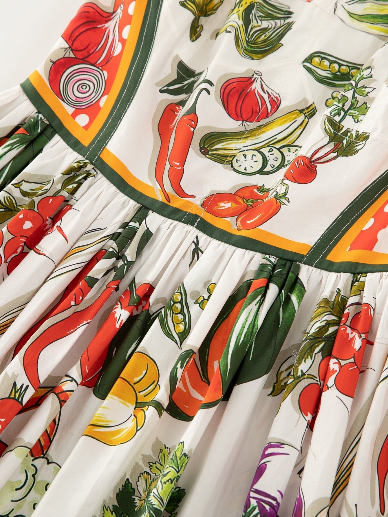 Colorful vegetable-print cotton dress with pleated skirt and vibrant red, green, and yellow accents. Perfect for summer.