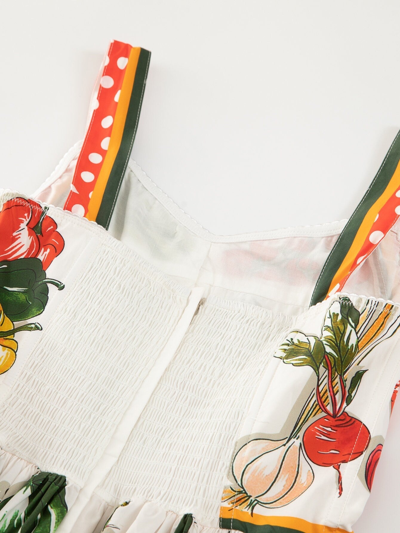 White smocked dress with colorful vegetable print and polka dot straps, perfect for summer styling.