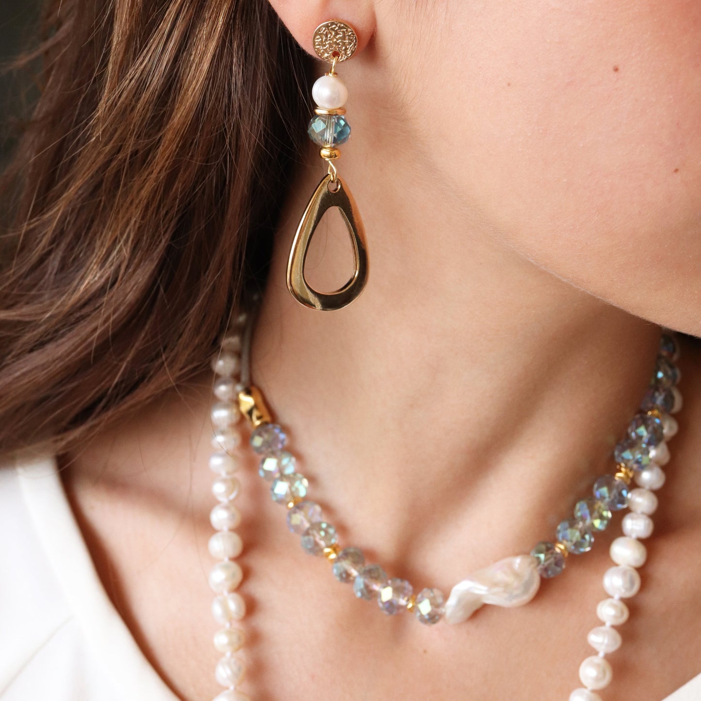 Pendientes dorados en forma de gota con perlas y cristal azul, combinados con un collar de perlas brillantes.