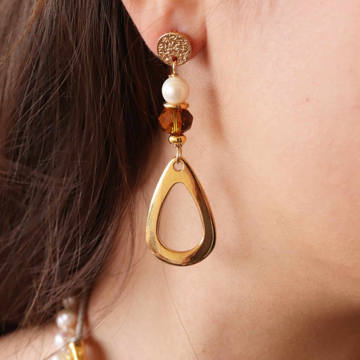 Pendientes dorados con perla blanca y detalle ámbar, diseño moderno y elegante.