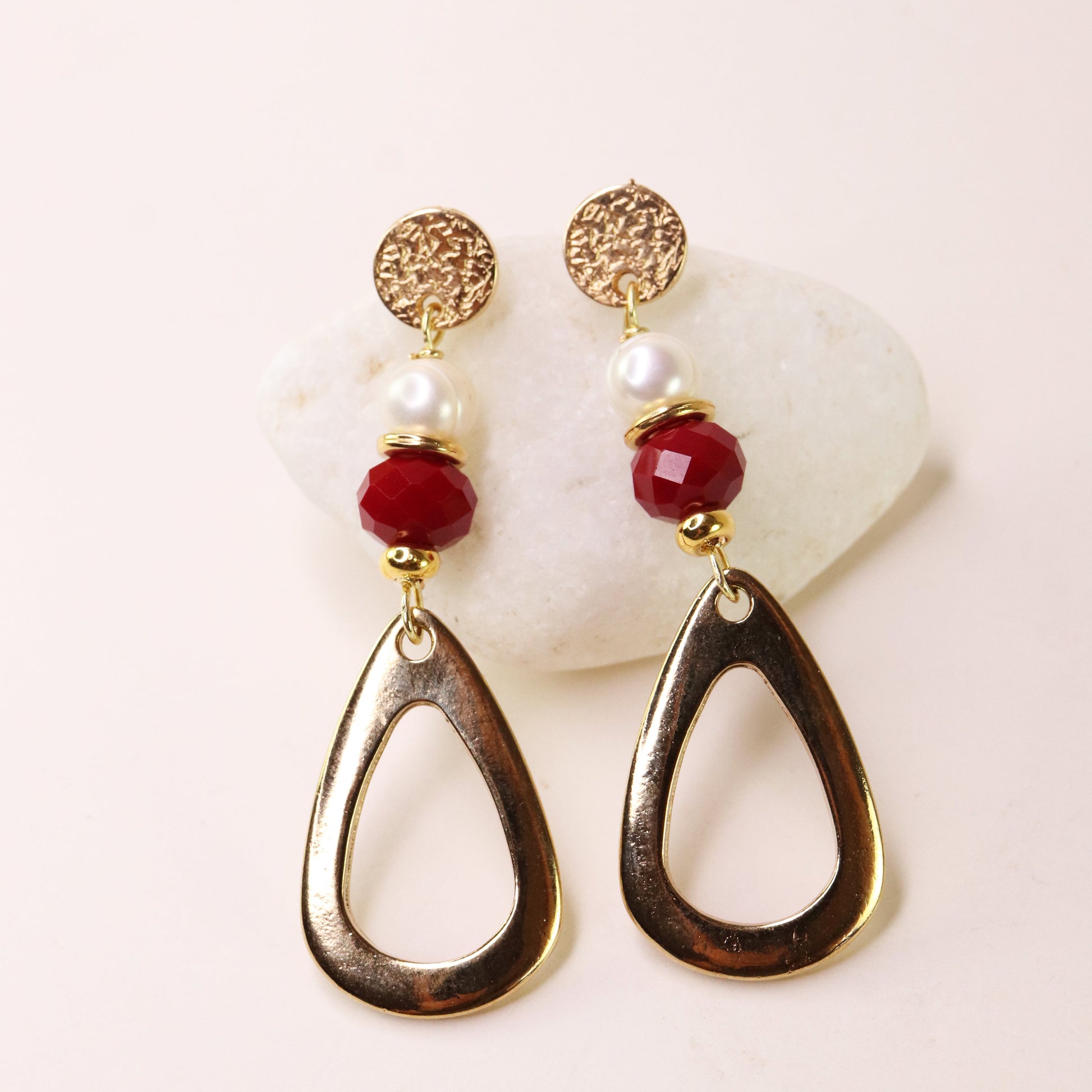 Pendientes dorados con perlas y cuentas rojas, diseño moderno y elegante, ideal para ocasiones especiales.