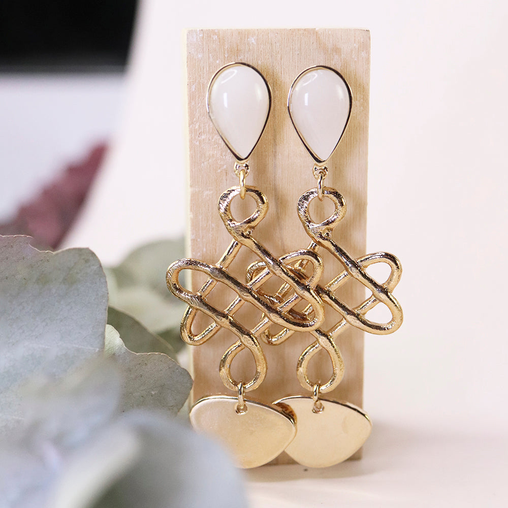 Pendientes dorados con forma de lazo y detalles en acrílico blanco, elegantes y modernos.
