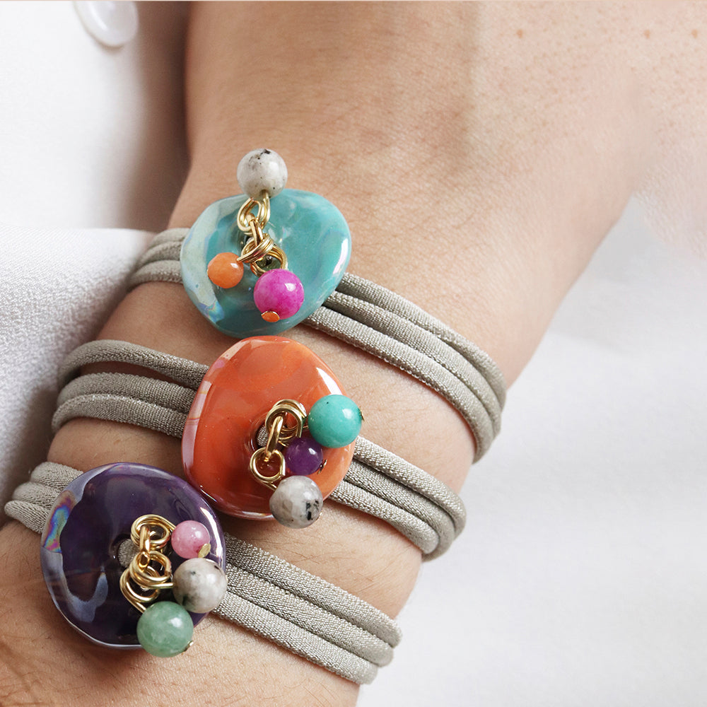 Pulseras de goma gris con cuentas de cerámica coloridas: azul, naranja, púrpura y verde. Estilo moderno y vibrante.