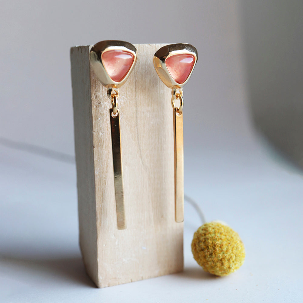 Pendientes dorados con piedra rosa en forma de triángulo y colgante dorado, estilo moderno y elegante.