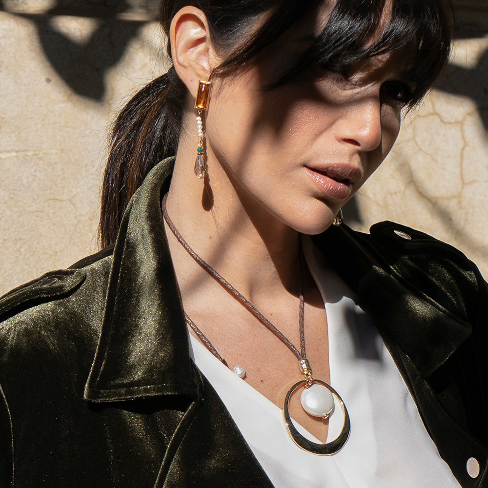 Collar de diseño con círculo dorado y piedra blanca, acompañado de aretes de cristal ámbar y detalles en verde.