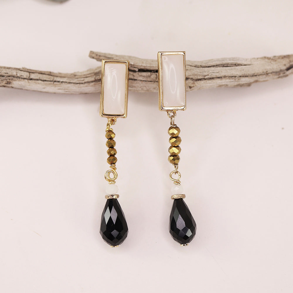 Pendientes largos de oro, con cristales marrones y gotas de cristal negro, estilo elegante y moderno.