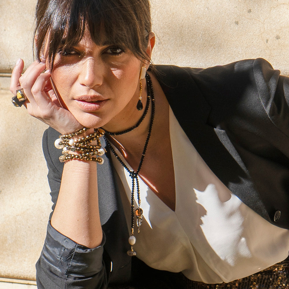 Mujer con chaqueta negra, blusa blanca y joyas doradas y negras en un look elegante y moderno.