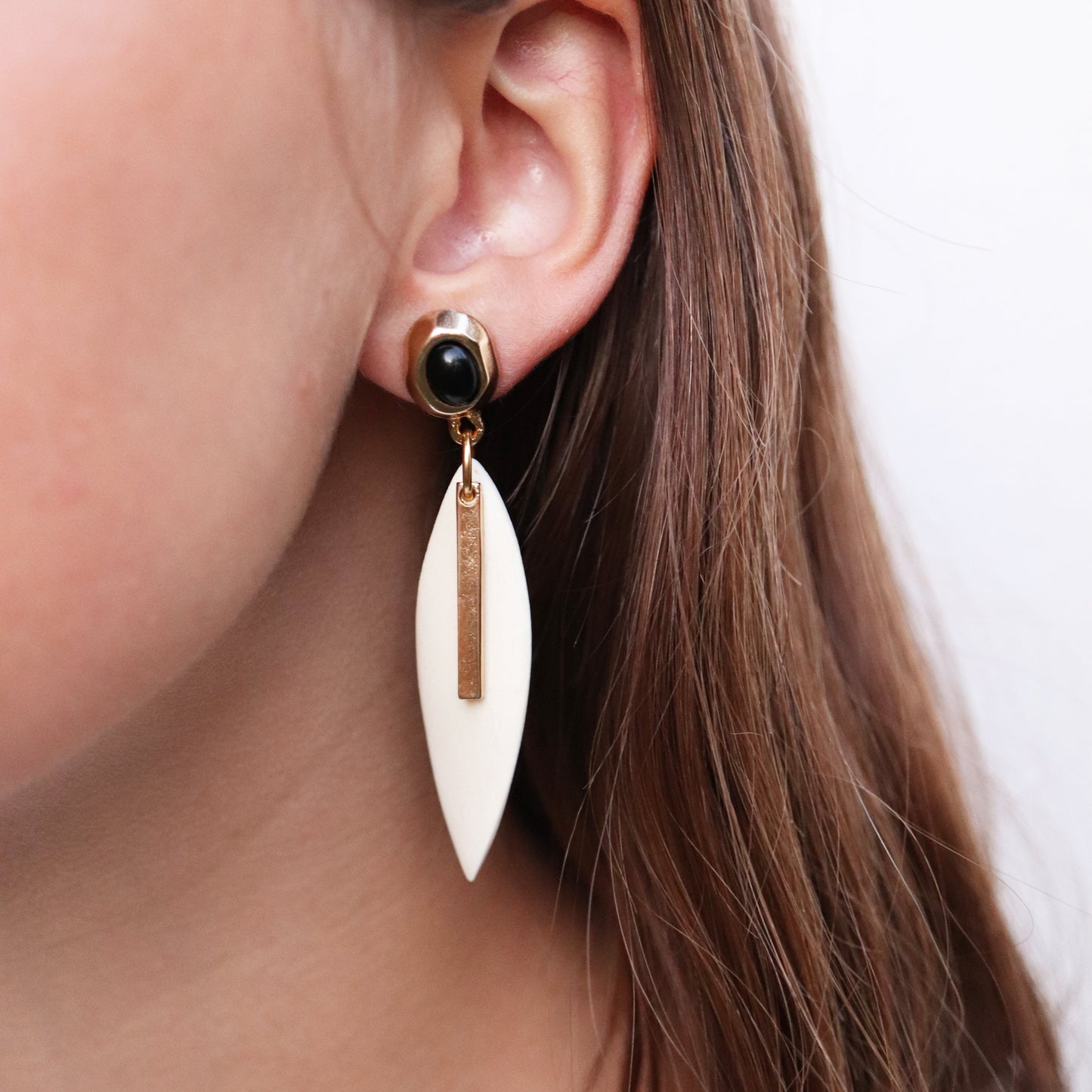 Pendientes largos de resina blanca con detalle dorado y piedra negra, estilo elegante y moderno.