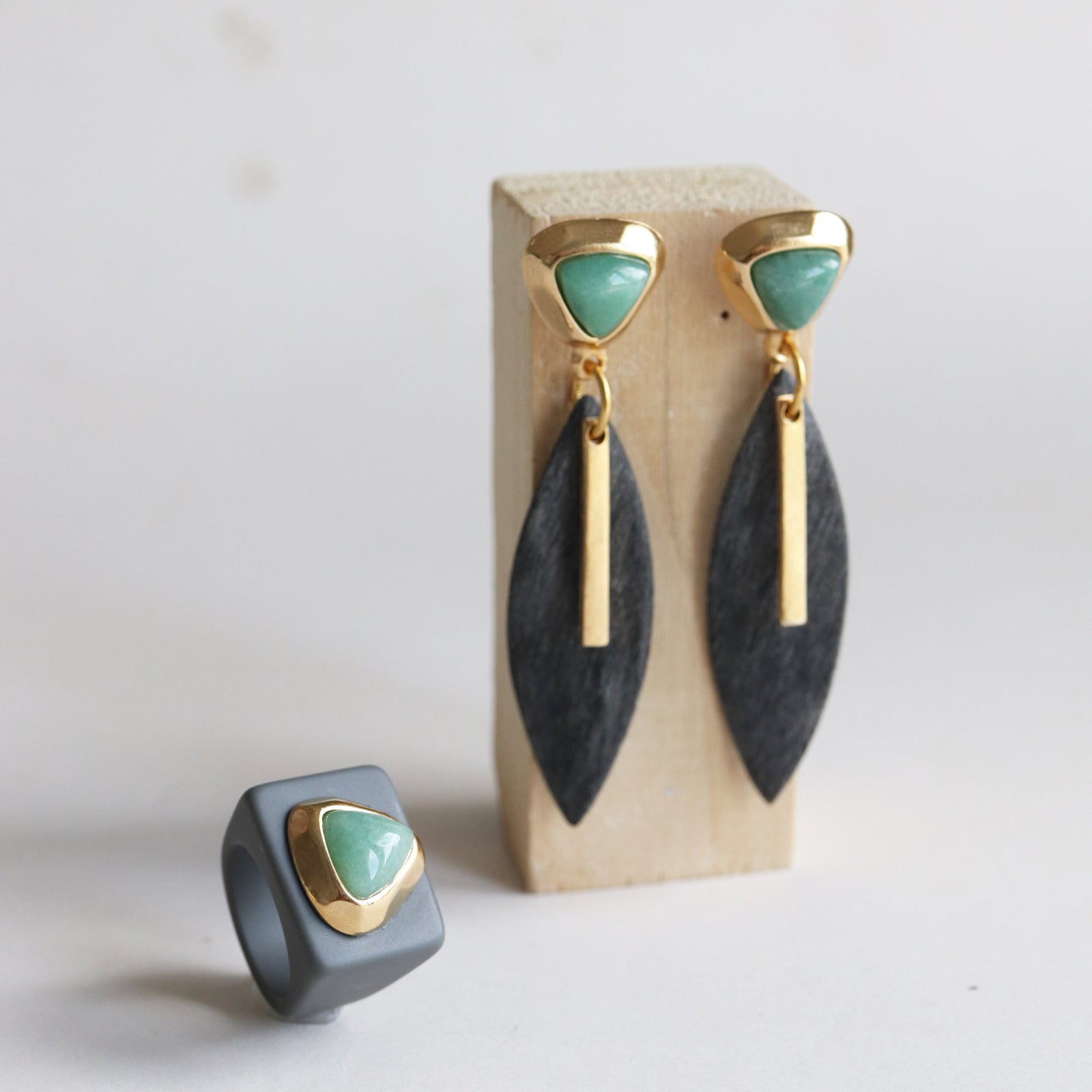 Pendientes de oro, verde y negro con diseño moderno, acompañados de un anillo gris y verde.