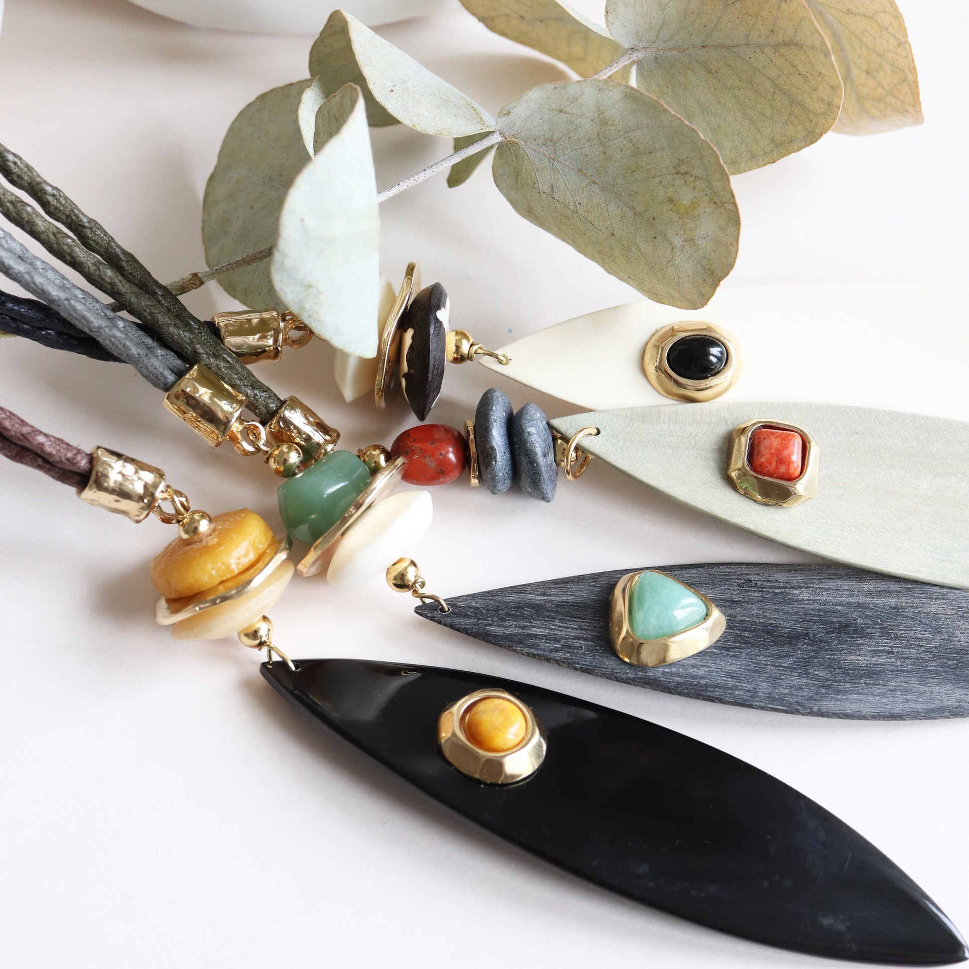Collares de diseño moderno, colores blanco, negro, verde y rojo, con detalles en oro y materiales naturales.