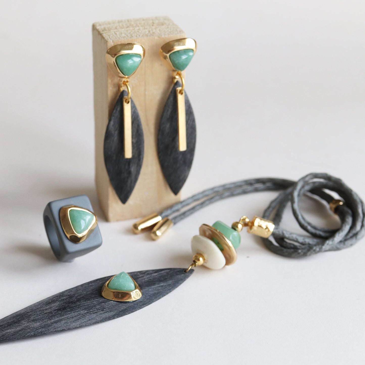 Pendientes de oro y verde, colgantes de hojas negras y anillo gris, combinación elegante y moderna de materiales.